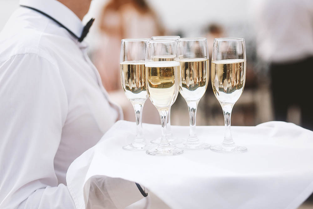 Waiter in white carries tray with champagne flutes